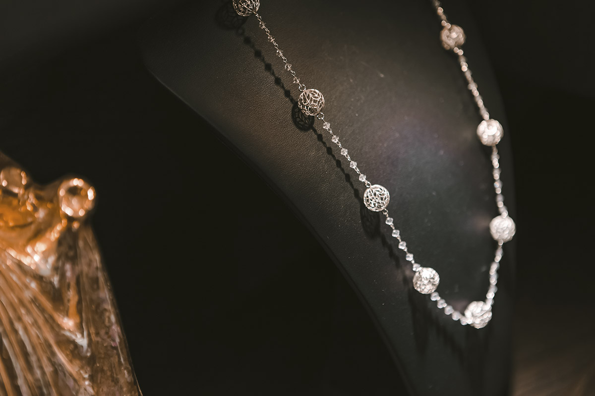 Collana in argento con i “bottoni” caratteristici dei costumi della tradizione abruzzese e catena con cristalli. Il collier, con i bottoni dalle trame sottili, rappresenta un lavoro di reinterpretazione: il maestro orafo Eugenio Di Rienzo segue il canone dell’innovazione applicandolo alle forme tipiche dei bottoni 