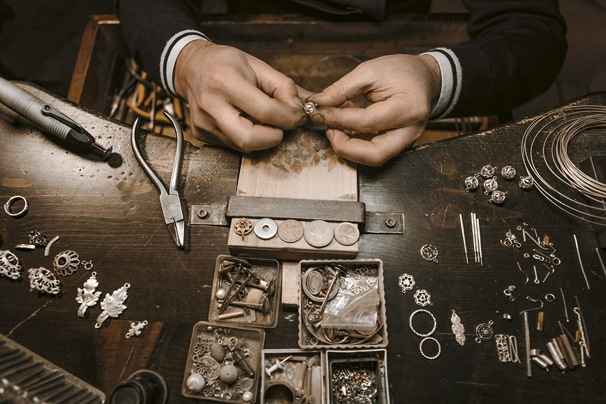 Al banco di lavoro, il maestro orafo crea prodigi con la filigrana: il suo laboratorio è artefice di sapienti gioielli sia in argento sia in oro. Si riconoscono i componenti di “Amorino”, iconica spilla-ciondolo tradizionale sul tema dell’amore (in basso a sinistra).